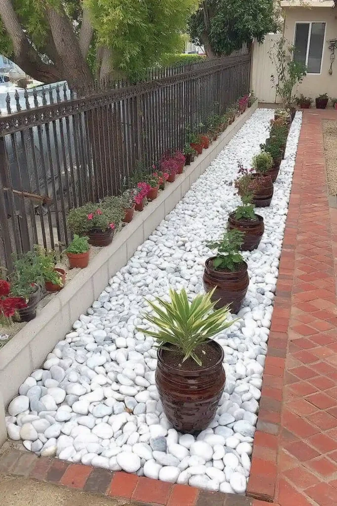 Fence line garden with pebbles and evenly spaced flower pots creating a neat pattern