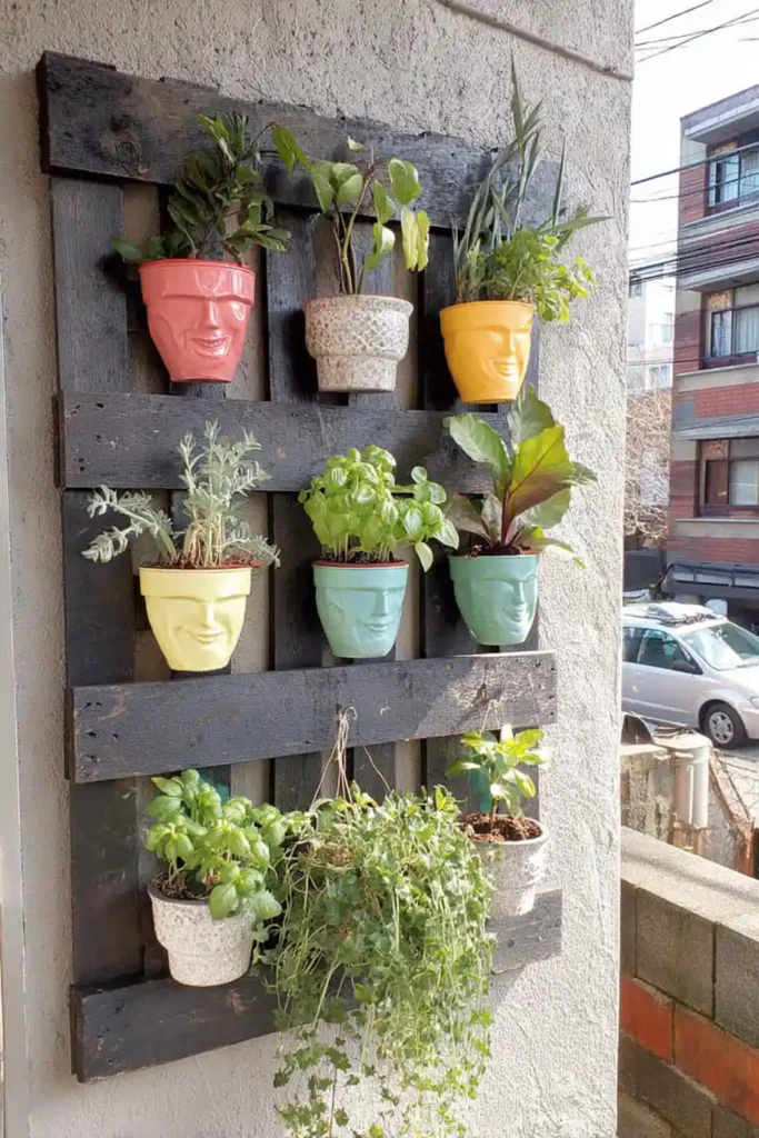 Black painted wall pallet garden with pastel pots and trailing herbs