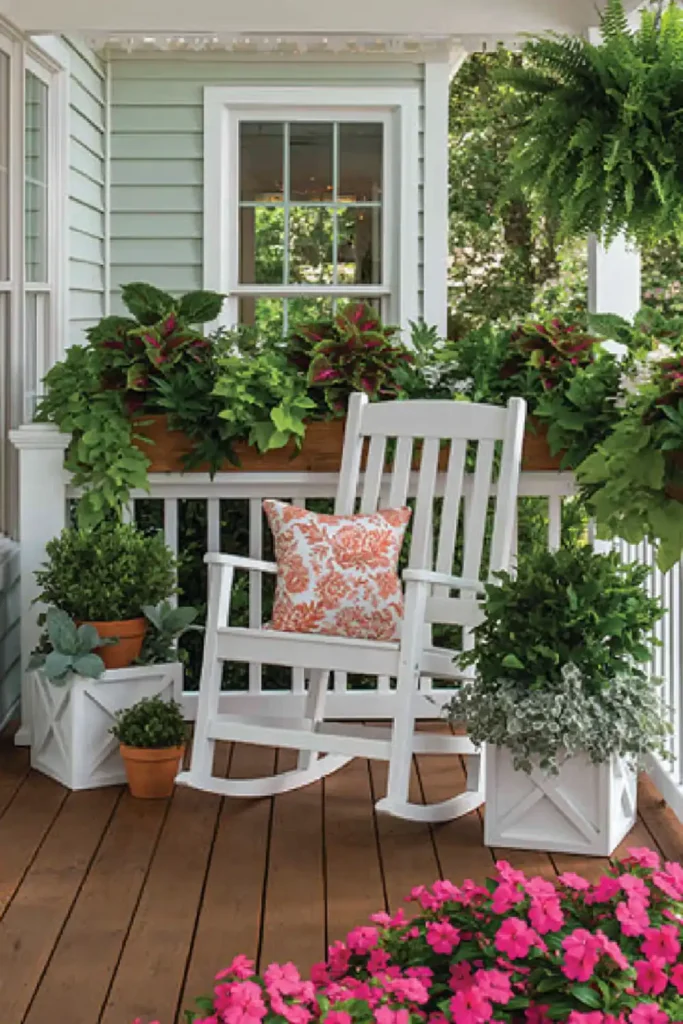 Shaded porch with a wood rocking chair, potted greenery, and pink flowers in the foreground