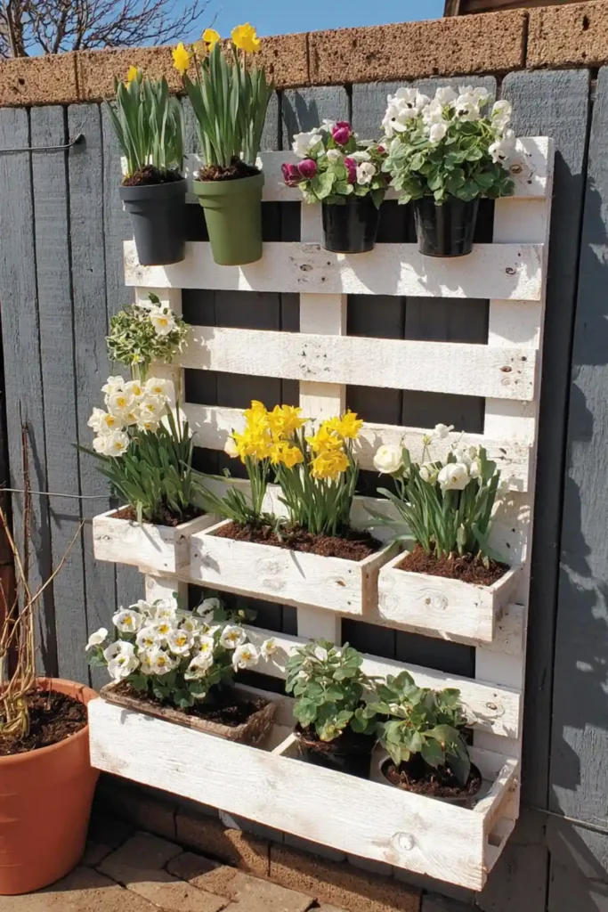 White floating pallet shelves displaying small flowers and planters on a gray wall