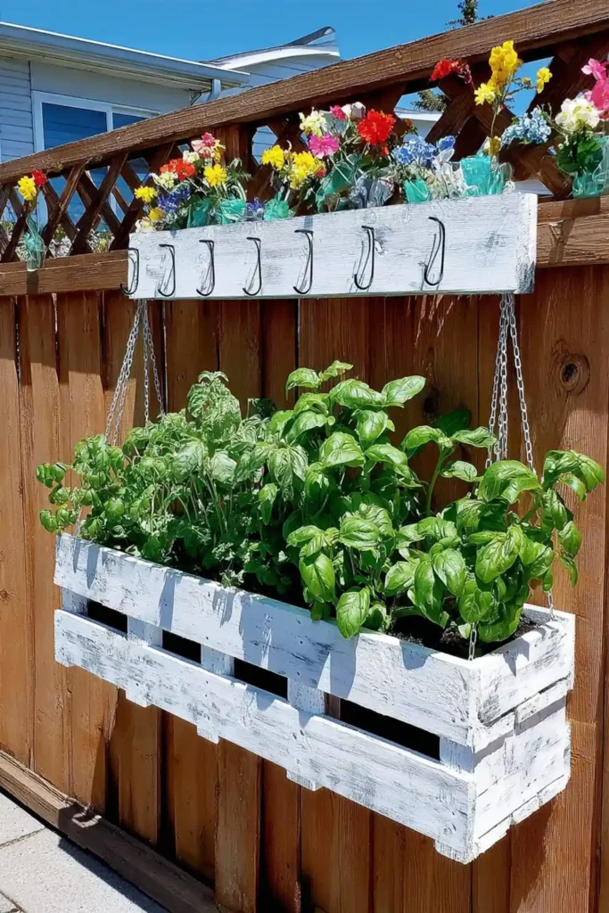 White hanging pallet planter on a backyard fence with leafy green plants
