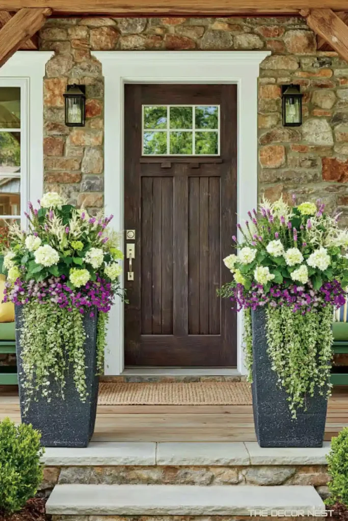 Two matching tall black porch planters with white blooms, purple flowers, and trailing greenery