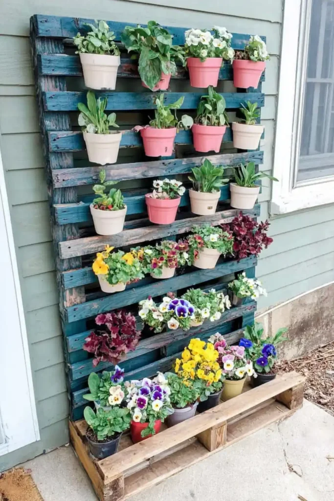 Purple vertical pallet garden with pink pots and bright flowers against siding