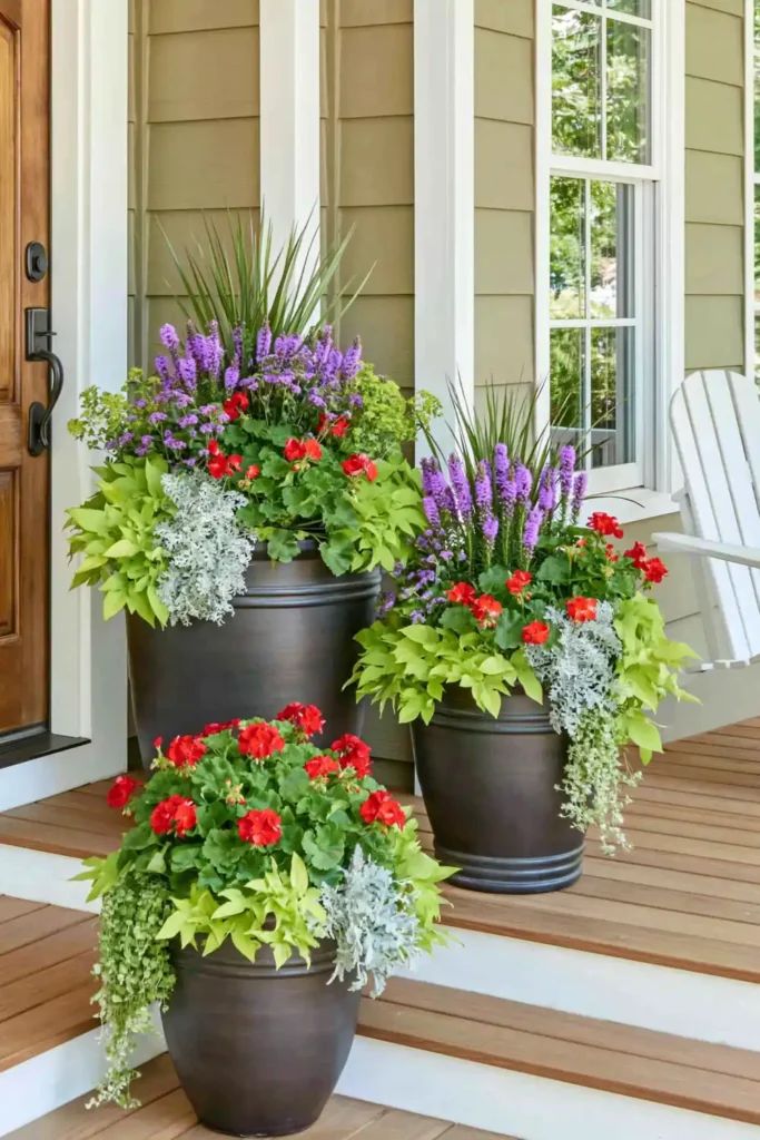 Two matching dark porch planters with red geraniums and purple flowers near front steps