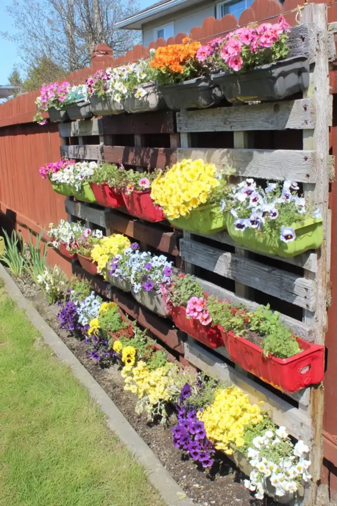 Dark vertical flower planters filled with bright blooms against a backyard fence