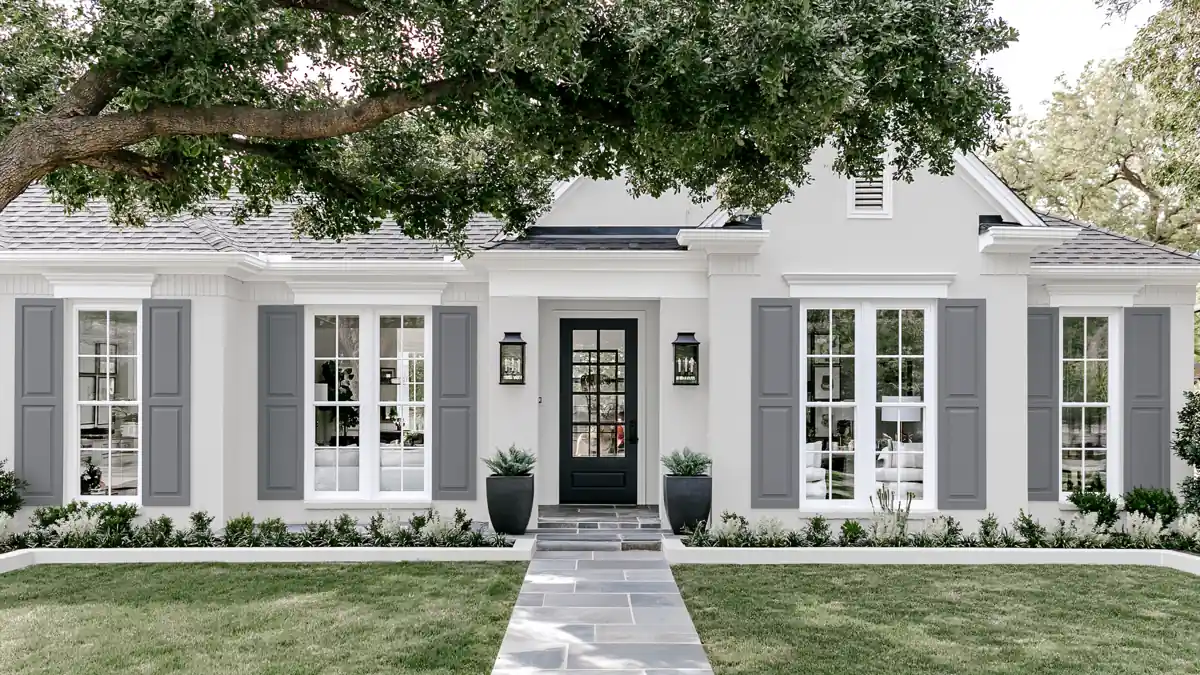 Classic Exterior Paint Color Combinations for a Timeless Home Look 1 Classic light stucco home exterior with pale taupe shutters, white-trimmed windows, dark planters, and a stone walkway.