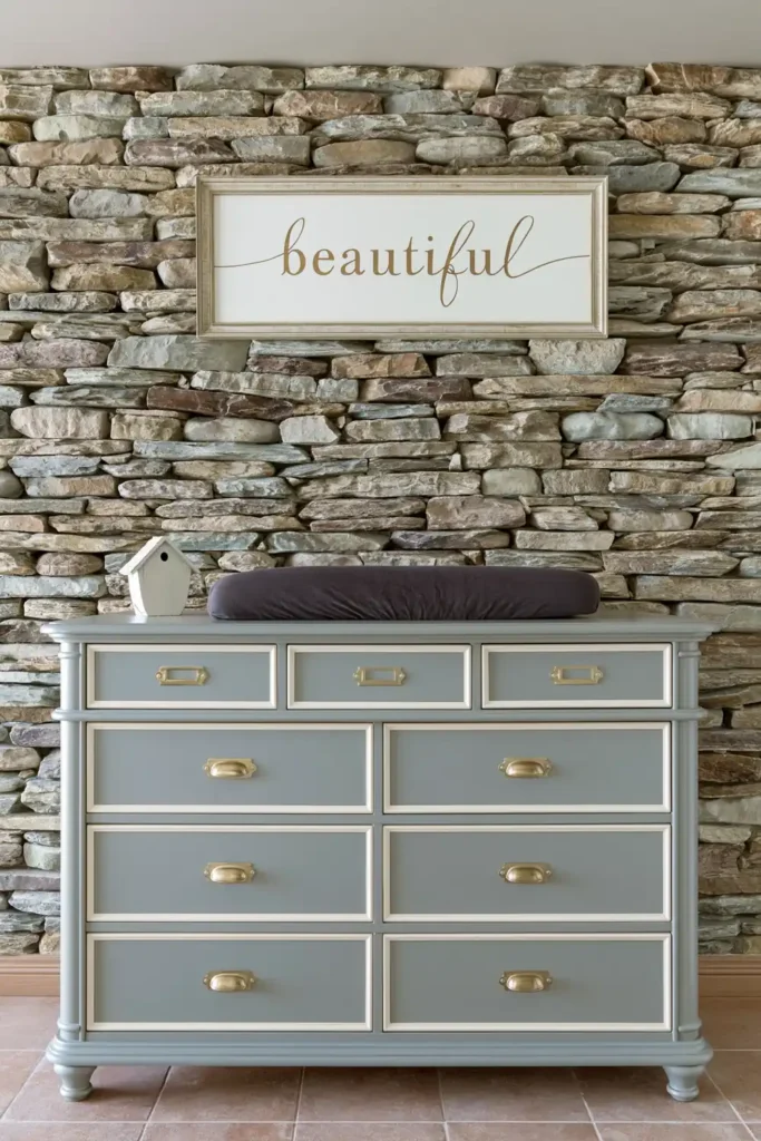 Gray dresser changing station with brass pulls and stacked stone wall in a nursery