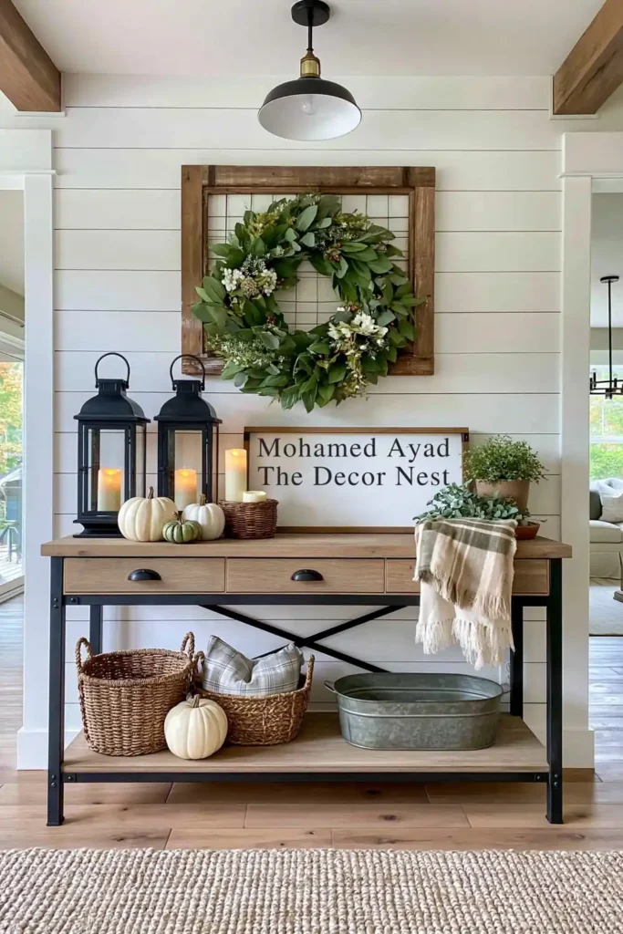 Industrial farmhouse console against white shiplap with black lanterns, candles, pumpkins, baskets, framed wreath, and autumn decor