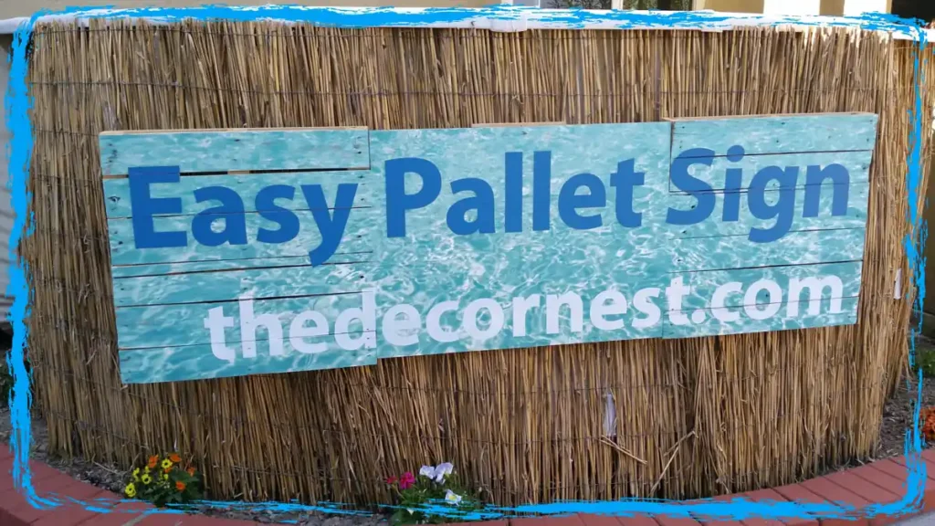 Reed-covered above-ground pool with a blue pallet sign, flowers, brick path, and casual backyard pool decor.