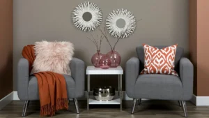 Warm beige-gray sitting area with gray chairs, orange accents, white side table, sunburst mirrors, and soft Off the Grid paint inspiration.