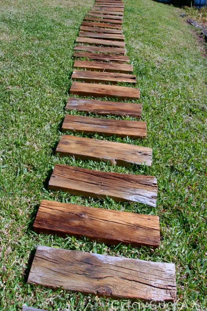 20 Budget-Friendly Outdoor Landscaping Ideas for a Charming Yard 10 Weathered wooden garden path crossing a green lawn for a simple outdoor landscaping idea.