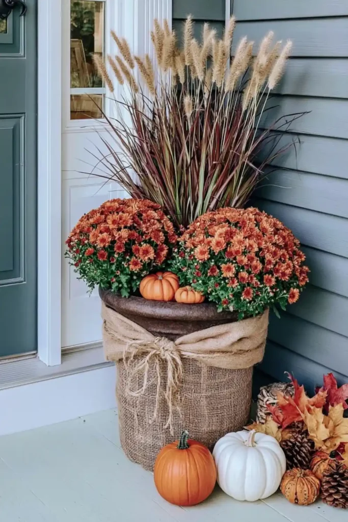 Rustic Fall Planters for the Front Porch That Bring Warm Autumn Charm 34 Rustic fall planter wrapped with burlap and twine, filled with orange mums, dried grasses, pumpkins, and fall leaves.