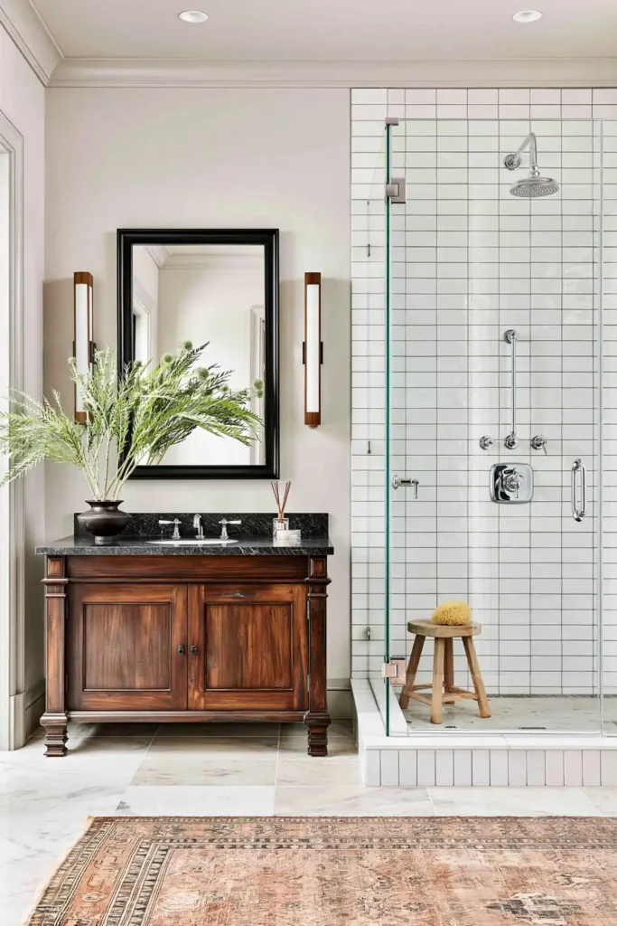 11 Spa-Inspired Bathroom Ideas on a Budget for a Calm, Restful Space 10 Calm bathroom with a reed diffuser, leafy stems, dark wood vanity, tiled glass shower, and warm patterned rug.