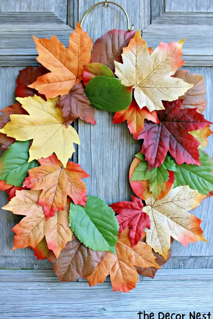 Colorful fall leaf wreath made with dense autumn leaves hanging against a weathered wood background.