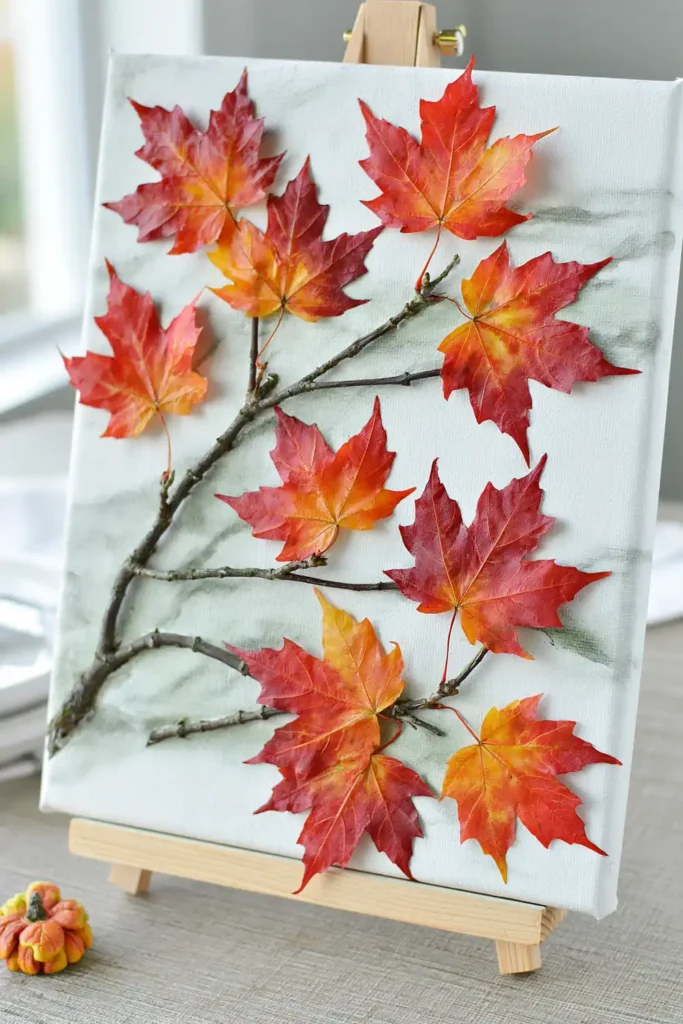 Fall canvas painting on a small easel with painted branches and red-orange maple leaves.