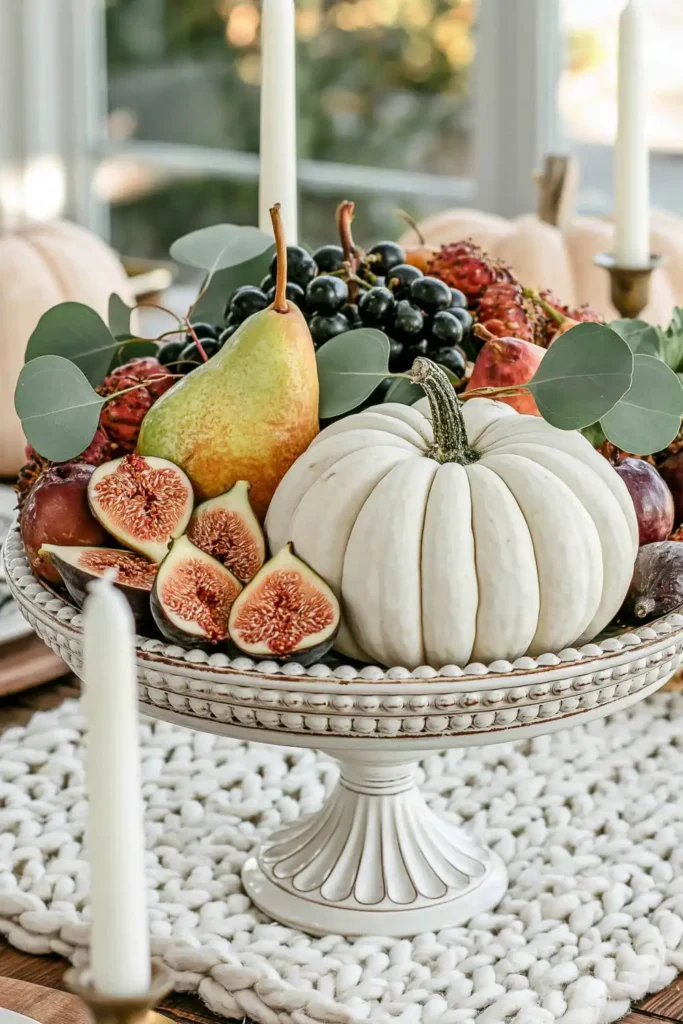 31 Fall Table Decor Ideas for Entertaining in a Warm, Seasonal Style 6 White pedestal bowl filled with a white pumpkin, pears, figs, grapes, colorful fruit, and eucalyptus leaves.