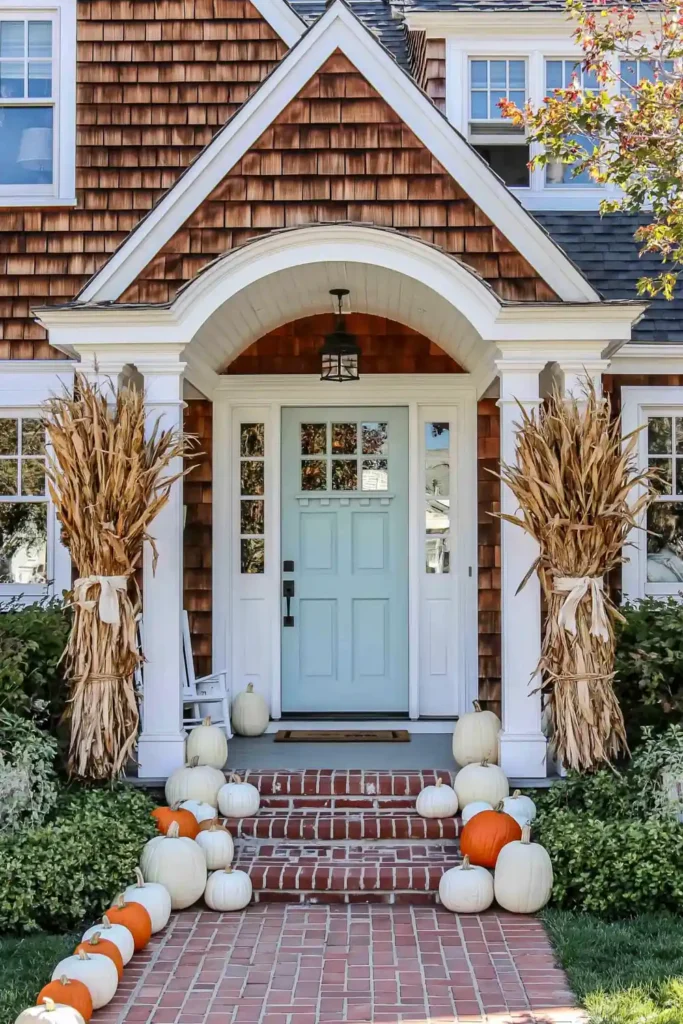 Neutral Halloween front porch decor with pale pumpkins, corn stalks, and a pale blue door.