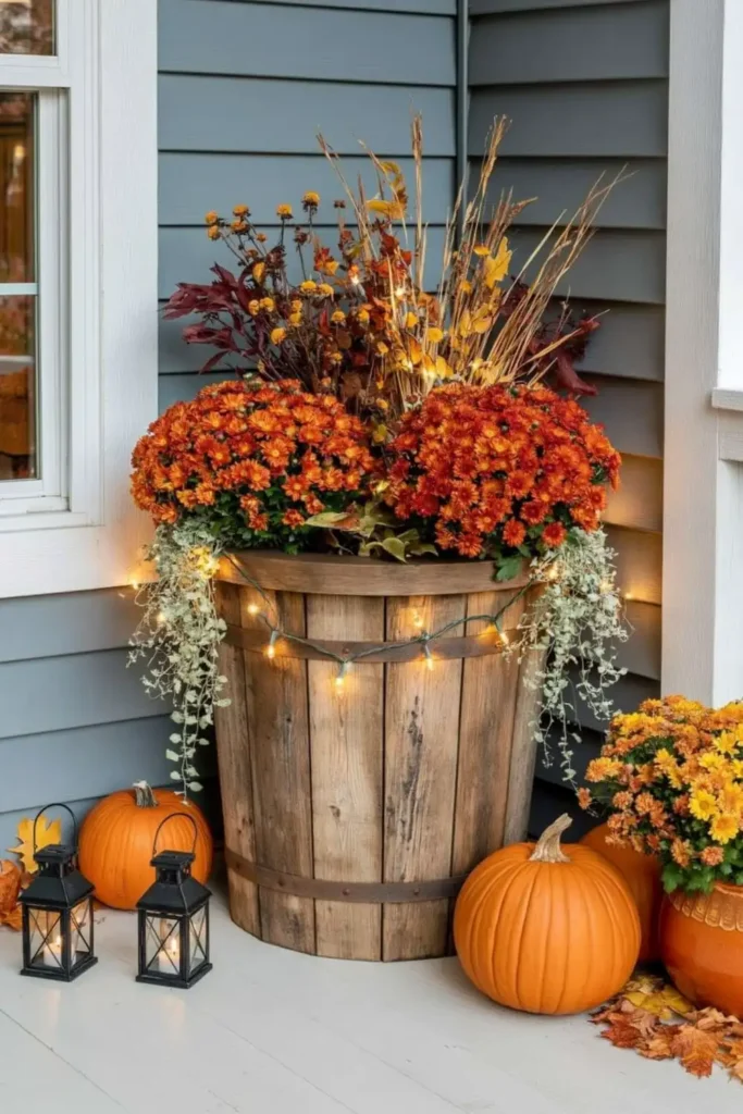 Rustic Fall Planters for the Front Porch That Bring Warm Autumn Charm 42 Rustic fall planter with LED fairy lights, orange mums, pumpkins, lanterns, and warm autumn porch lighting.