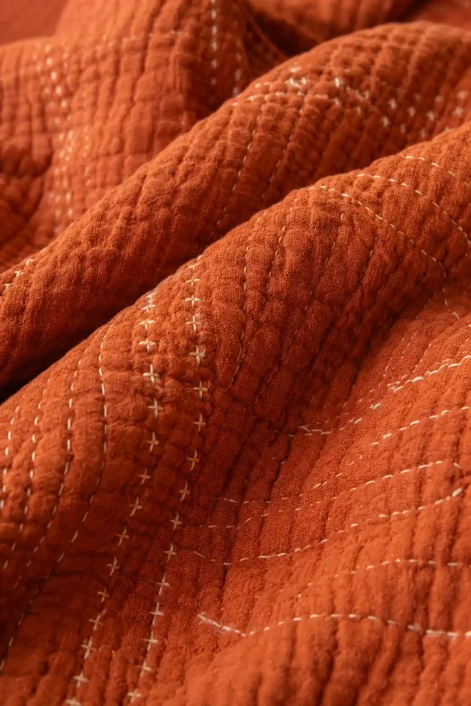 Close-up of a rust-orange textured blanket with stitched details for warm autumn bedroom decor