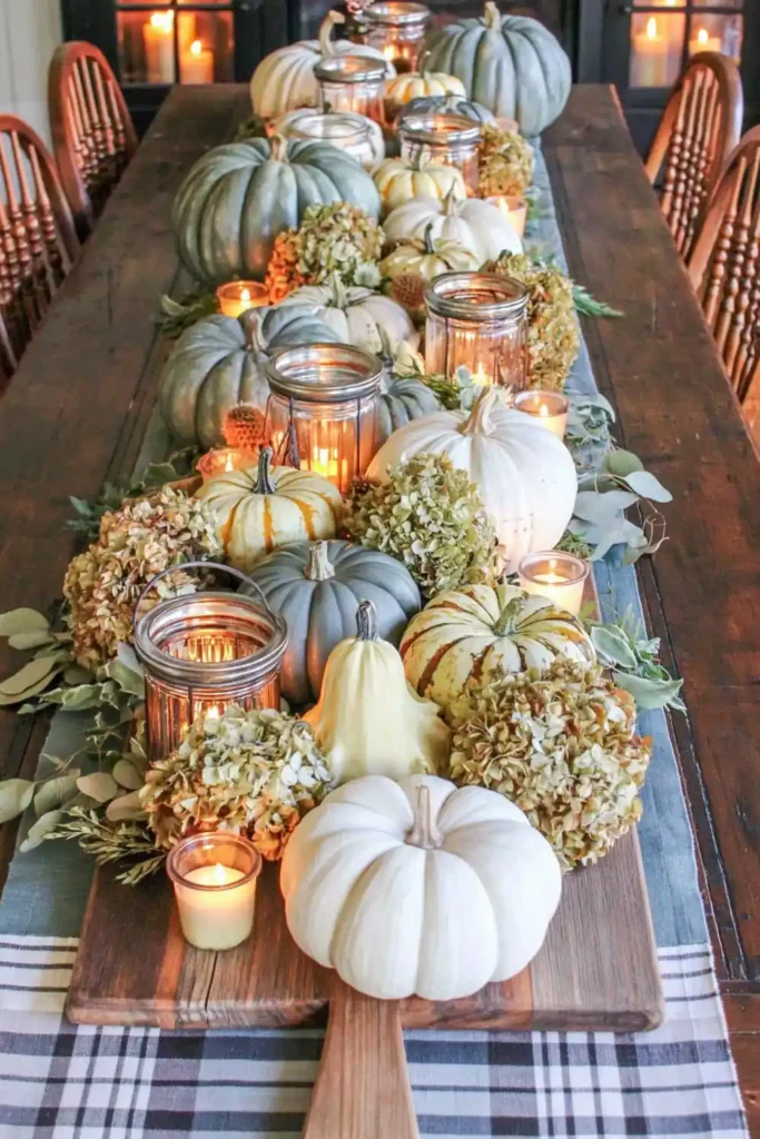 31 Fall Table Decor Ideas for Entertaining in a Warm, Seasonal Style 25 Wooden pizza board centerpiece with pale pumpkins, gourds, dried hydrangeas, greenery, votive candles, and glass lanterns.