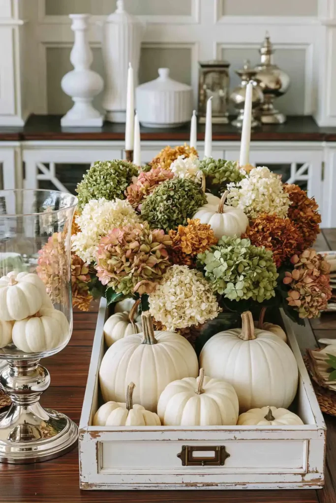 31 Fall Table Decor Ideas for Entertaining in a Warm, Seasonal Style 16 Weathered white wooden caddy filled with dried hydrangeas and white pumpkins beside a glass hurricane of miniature pumpkins.
