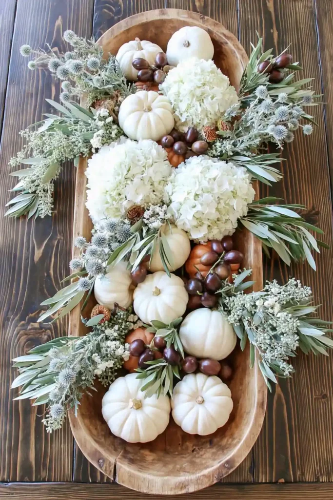 31 Fall Table Decor Ideas for Entertaining in a Warm, Seasonal Style 27 Wooden dough bowl filled with olive branches, dark olives, white hydrangeas, and small white pumpkins.