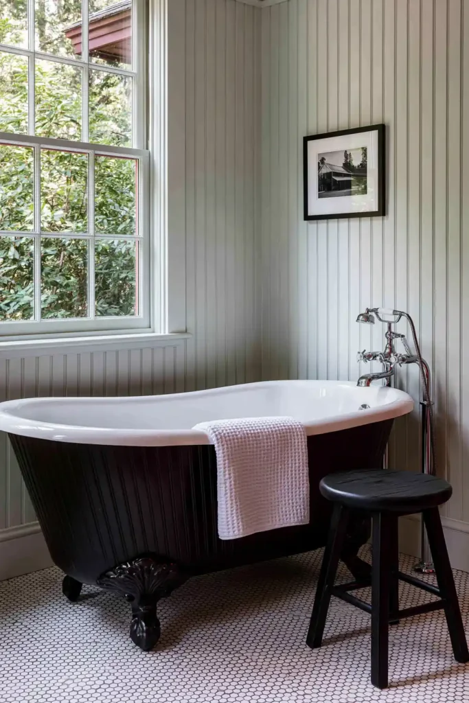 30 Modern Farmhouse Bathroom Decor Ideas for a Warm, Updated Space 11 Classic farmhouse bathroom with a black clawfoot tub, white shiplap walls, hex tile floor, and framed black-and-white artwork.