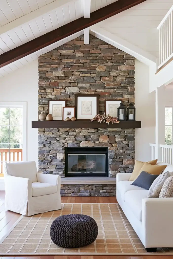 Cozy open living room with a stone fireplace, white sofa and armchair, geometric rug, and dark knitted pouf.
