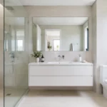 Bright small bathroom with light neutral tiles, a floating vanity, large mirror and clear glass shower screen.