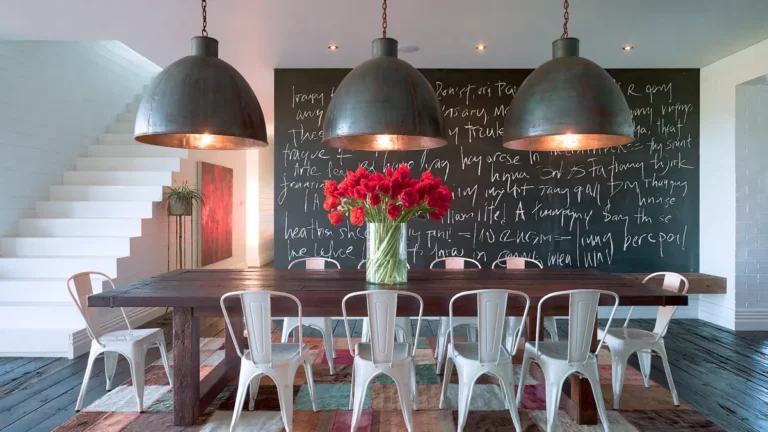 Dining Room Lighting Ideas to Create the Perfect Mood 37 Industrial dining room with three oversized dark grey pendant lights above a wooden table, white metal chairs, red flowers, and a chalkboard wall.