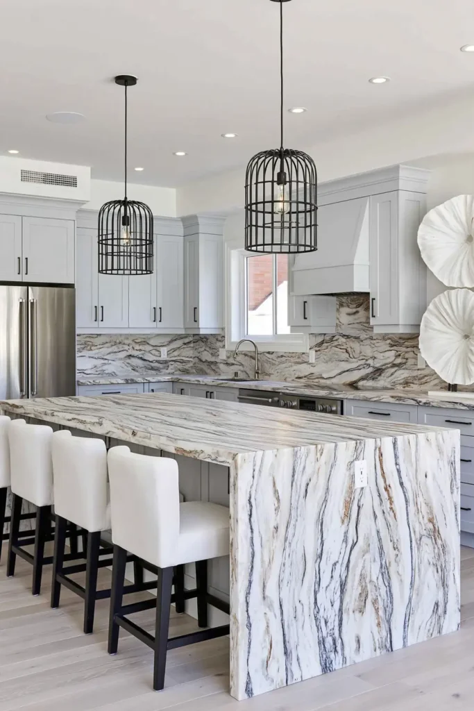 Matching pale veined porcelain surfaces across a kitchen backsplash, countertops, and waterfall island.