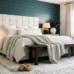 Modern farmhouse bedroom with a deep teal shiplap wall, cream tufted headboard, layered neutral bedding, wooden bench, and ivory fringe rug.