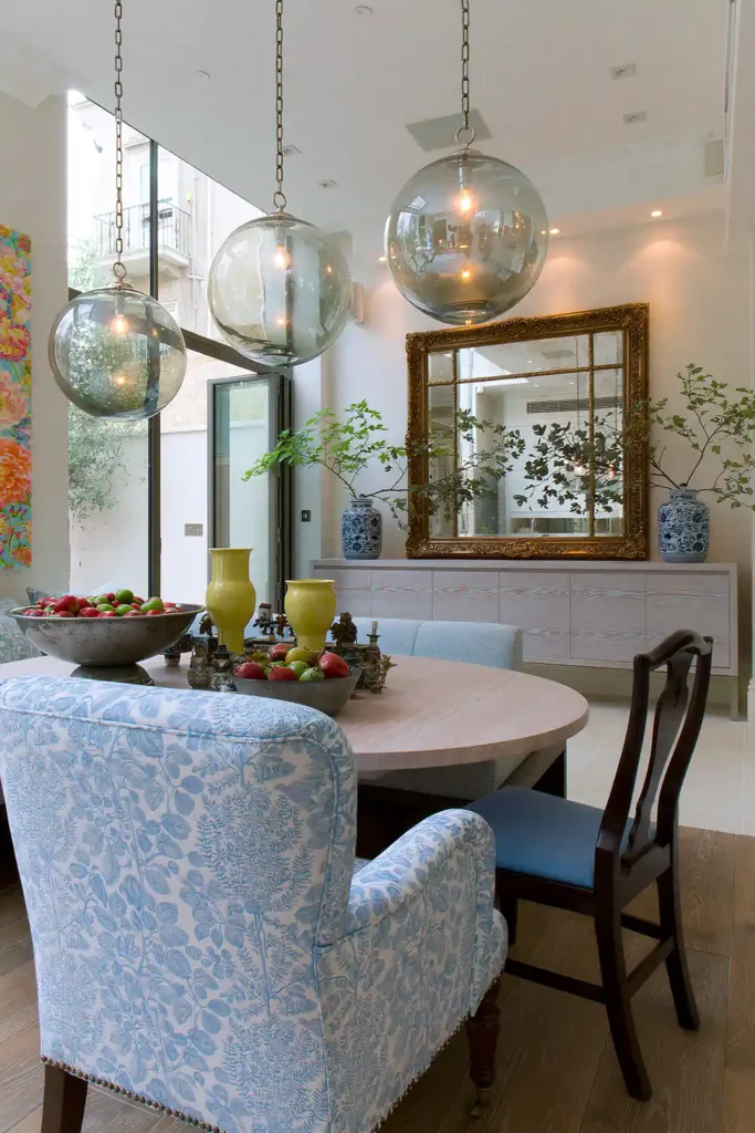 Dining Room Lighting Ideas to Create the Perfect Mood 4 Smoke-gold glass globe pendants at staggered heights above a round wooden dining table with colorful collected decor.
