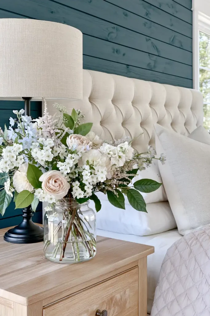 Modern Farmhouse Bedroom Ideas for a Warm, Relaxed Retreat 8 Spring flower arrangement in a glass jar on a maple nightstand beside neutral modern farmhouse bedding.