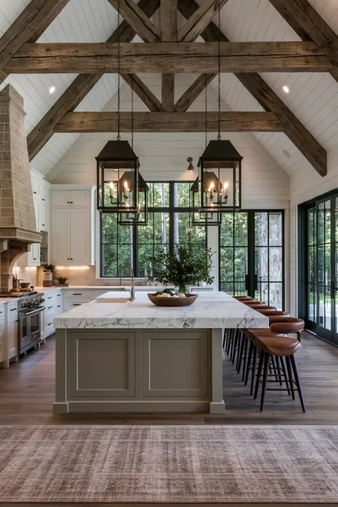 29 Barndominium Kitchen Designs for Rustic, Modern, and Timeless Spaces 22 High-ceiling barndominium kitchen with weathered timber trusses, oversized black lantern pendants, a pale gray island, leather stools, and dark wood flooring.