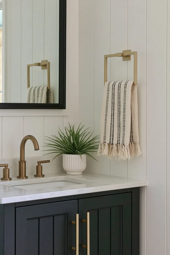 21 Guest Bathroom Decorating Ideas for a Friendly Space 4 Small neutral guest bathroom with a black vanity, gold fixtures, striped hand towel, and white paneled walls.
