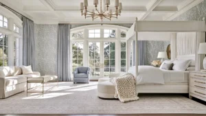 Bright bedroom with a white four-poster bed, cream seating, blue-gray curtains, aqua botanical wallpaper, and a gold chandelier.