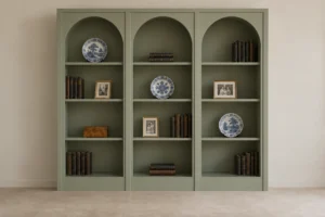 Arched built-in bookcase in muted sage with three display bays, books, family photos, and porcelain plates