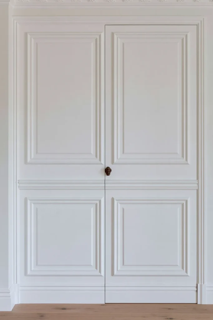 18 Secret Door Ideas That Fit Beautifully Into Your Home 17 White deep-paneled classic jib door with layered moldings, a bronze knob, and pale wood flooring.