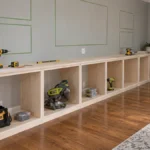 Unfinished DIY family room built-in shelves with pale plywood base cabinets, a light wood countertop, tools, hardwood flooring, and a white fireplace surround.