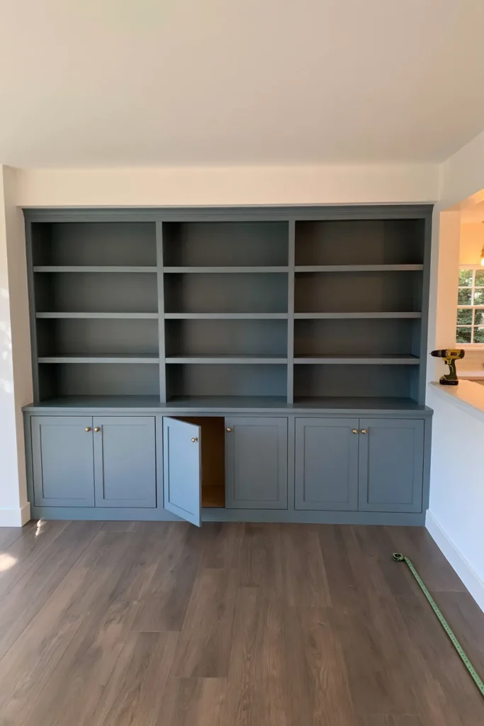 DIY IKEA Billy Bookcase Library Wall Ideas for a Custom Built-In Look 3 Teal Billy bookcase built-in with open shelving, Shaker-style lower cabinet doors, brass knobs, and cabinet installation tools.
