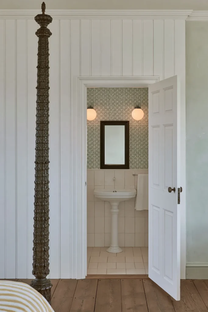 18 Secret Door Ideas That Fit Beautifully Into Your Home 8 White wainscoting secret door opening from a traditional bedroom into a small bathroom with green patterned wallpaper.