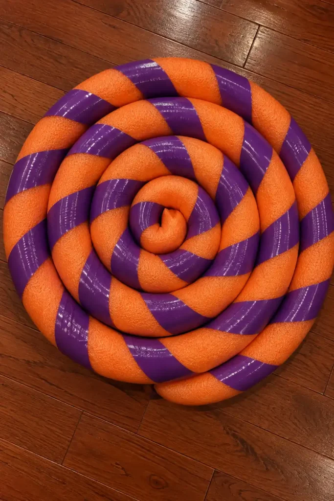 DIY Giant Lollipops Holiday Decor for a Candyland Display 2 DIY giant lollipop candy spiral made from orange foam pool noodles and purple duct tape on a wooden floor.
