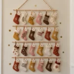 Handmade DIY heirloom Advent calendar wall decor featuring 24 colorful embroidered felt stockings, numbered wooden stars, natural wood dowels, and decorative beads.
