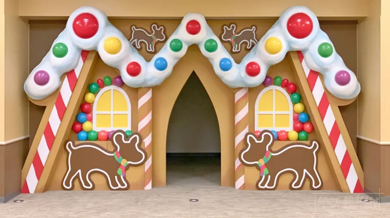 DIY Life-Sized Gingerbread House Outdoor Decor: 9 Creative Ideas for a Candy-Inspired Display 11 Life-sized gingerbread house entrance with a snowy white roof, red-and-white peppermint columns, colorful gumballs, yellow windows, and oversized gingerbread cookie decorations.