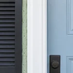 Pale blue front door with dark charcoal shutter, white trim, and a light-green foam strip prepared for fall decorating.