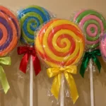 Cluster of oversized wrapped spiral lollipops with colorful bows displayed against a beige wall.
