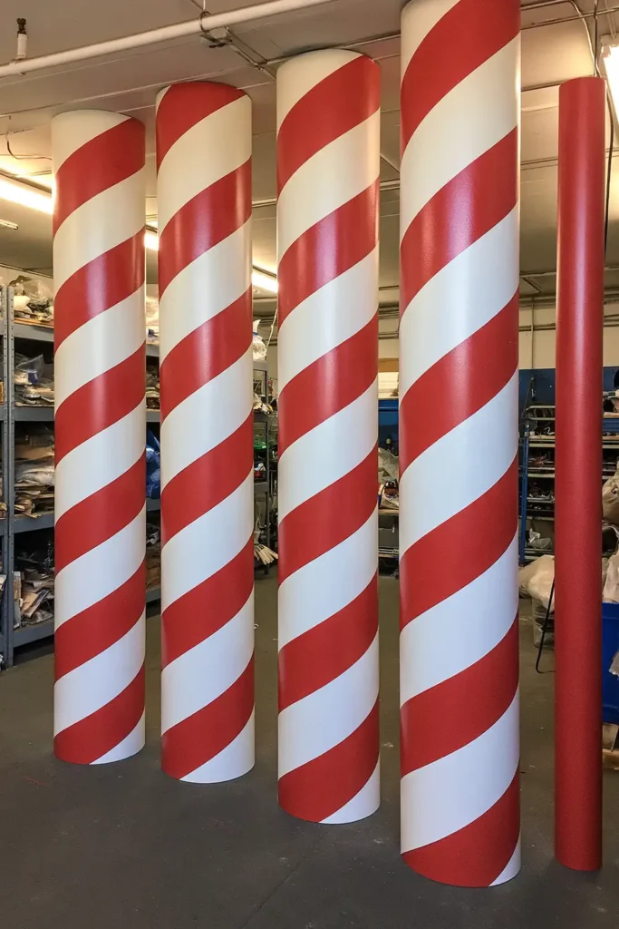Tall DIY peppermint columns with glossy red-and-white spiral stripes standing upright in an indoor workshop.