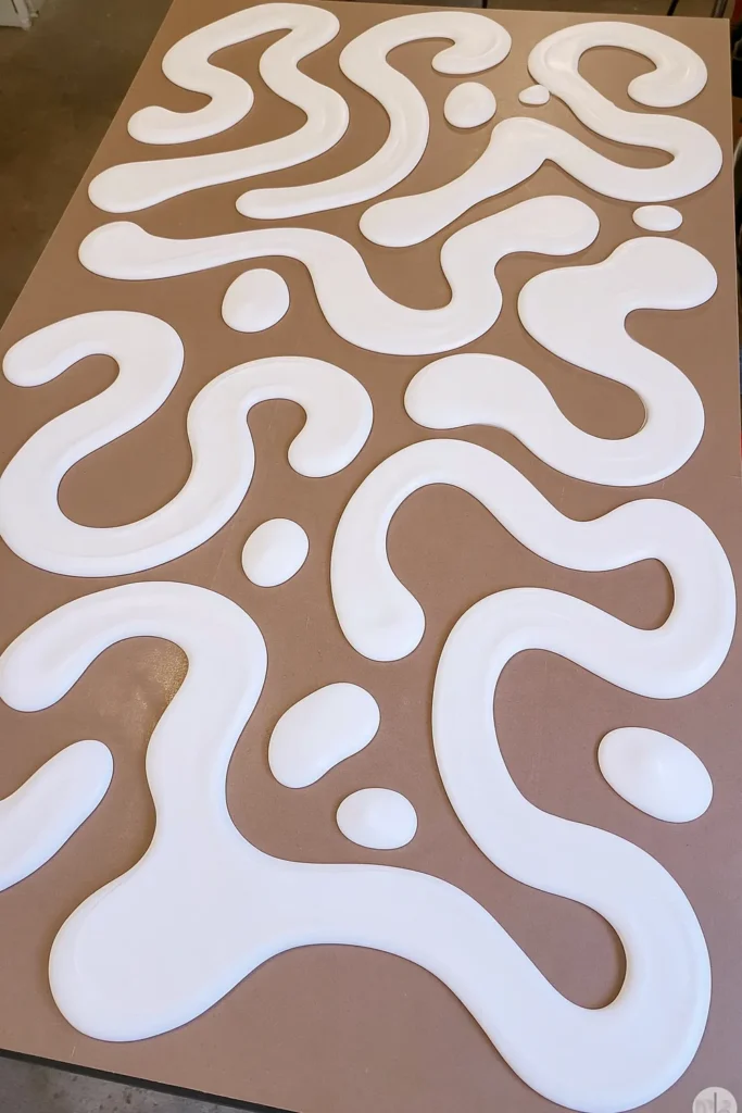 Thick raised white icing-style decorations arranged in curved lines, loops, and rounded dollops across a brown craft surface.