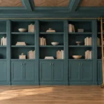 DIY IKEA Billy bookcase library wall painted teal with lower doors, brass knobs, trim, crown moulding, and a rolling ladder